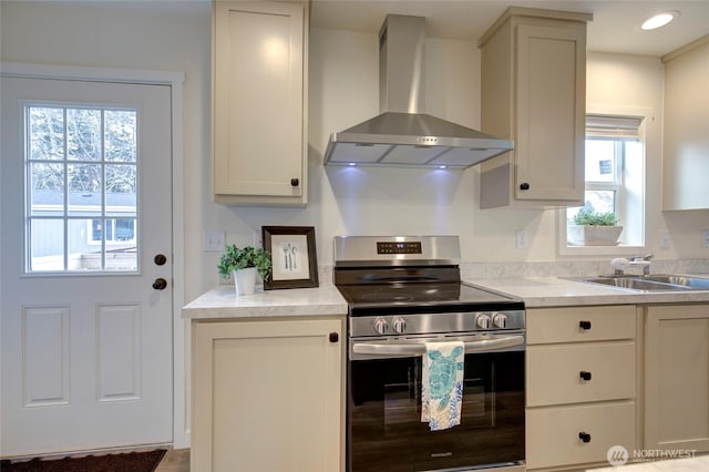 kitchen with light countertops, wall chimney range hood, a sink, and stainless steel range with electric cooktop