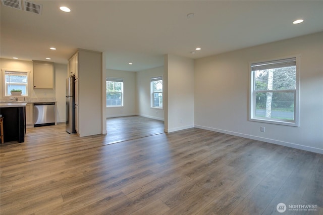 unfurnished living room with a healthy amount of sunlight, light wood-style floors, and visible vents