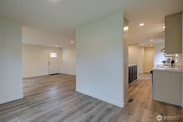 unfurnished room with recessed lighting, visible vents, light wood-style flooring, a sink, and baseboards