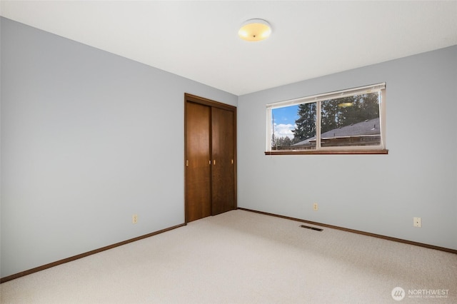 unfurnished bedroom with baseboards, visible vents, a closet, and light colored carpet