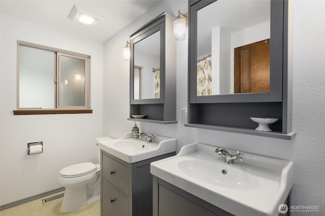 bathroom featuring toilet, two vanities, a sink, and visible vents