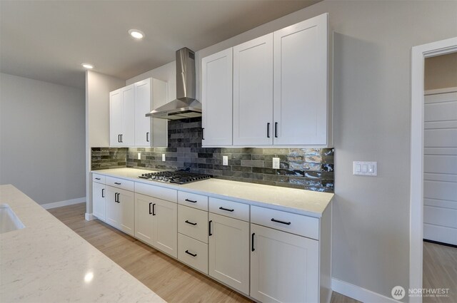 20907 150th St E Unit 1460, Bonney Lake, WA 98391 - kitchen featuring white cabinets, light wood-style floors, wall chimney range hood, backsplash, and stainless steel gas stovetop