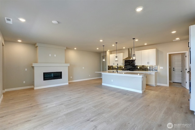20907 150th St E Unit 1460, Bonney Lake, WA 98391 - kitchen featuring light wood finished floors, recessed lighting, backsplash, a glass covered fireplace, and wall chimney exhaust hood