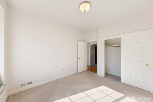 unfurnished bedroom with a closet, visible vents, light carpet, and baseboards