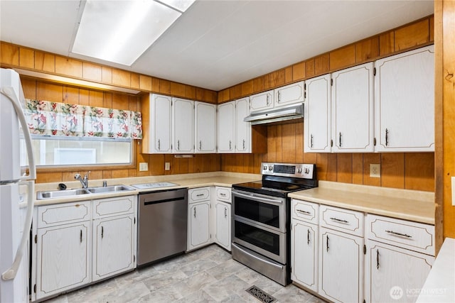 kitchen with wooden walls, under cabinet range hood, stainless steel appliances, a sink, and light countertops