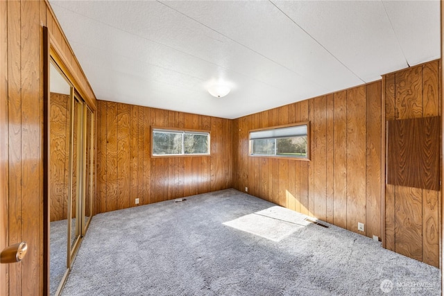 carpeted spare room with wooden walls and visible vents