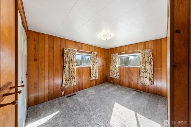 spare room with wood walls, carpet flooring, and visible vents