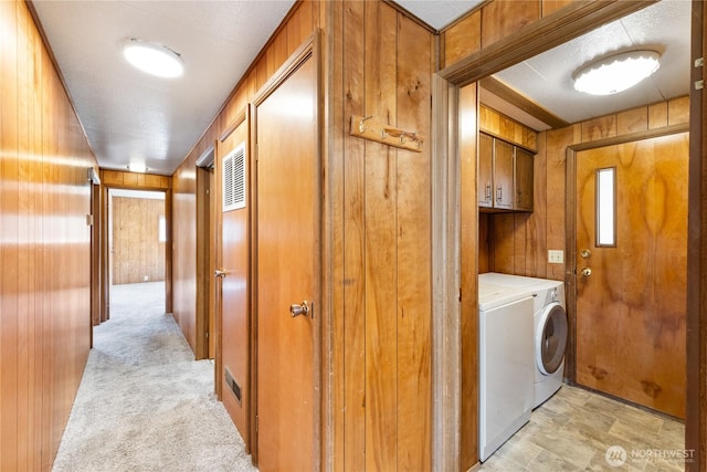 washroom featuring light carpet, separate washer and dryer, cabinet space, and wooden walls