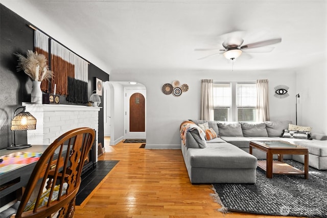 living area with light wood finished floors, baseboards, arched walkways, ceiling fan, and a fireplace