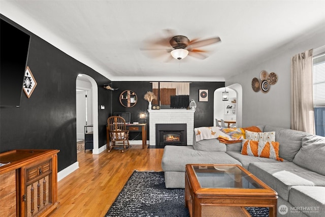 living room featuring arched walkways, baseboards, ceiling fan, light wood-style floors, and a fireplace