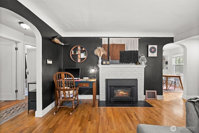 living room featuring arched walkways, a brick fireplace, visible vents, and wood finished floors