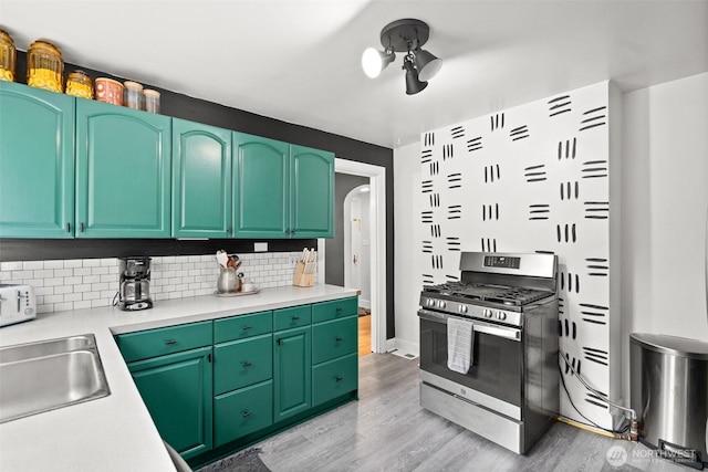 kitchen with light countertops, light wood finished floors, stainless steel range with gas stovetop, and decorative backsplash