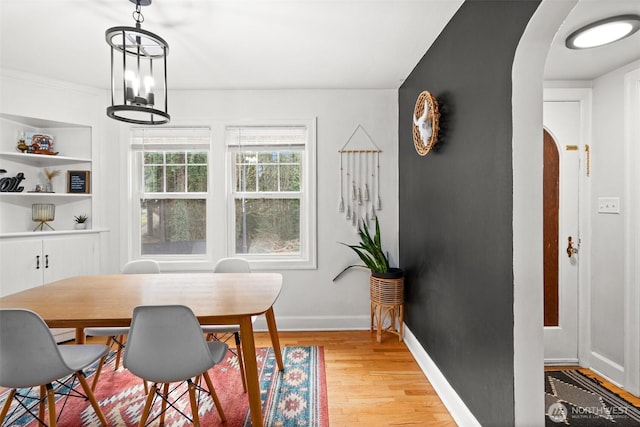 dining space with built in features, arched walkways, a chandelier, light wood-type flooring, and baseboards