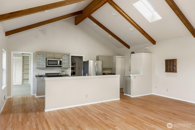 kitchen with high vaulted ceiling, gray cabinetry, a skylight, appliances with stainless steel finishes, and light wood finished floors