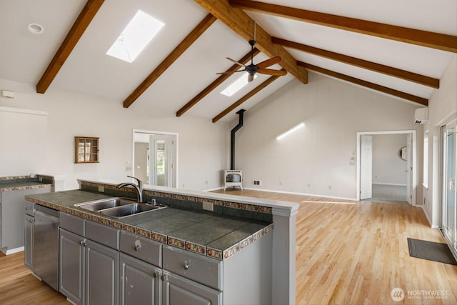 kitchen featuring tile countertops, gray cabinets, a wood stove, a sink, and dishwasher