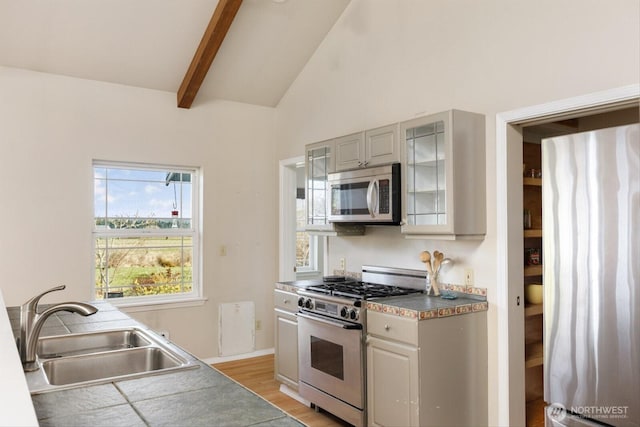 kitchen featuring lofted ceiling with beams, stainless steel appliances, a sink, gray cabinets, and glass insert cabinets