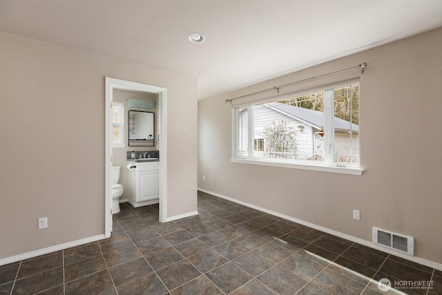 unfurnished bedroom with ensuite bathroom, a wall unit AC, a sink, visible vents, and baseboards