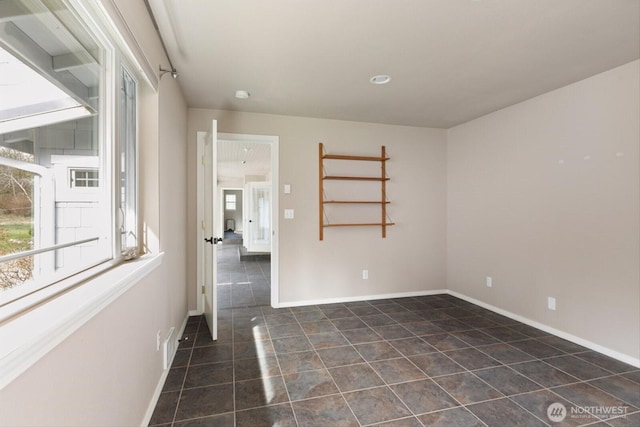 empty room featuring baseboards and dark tile patterned flooring