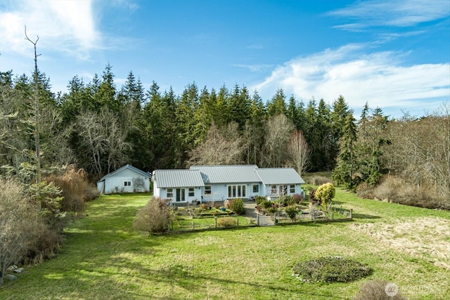 view of front of home featuring metal roof, a front lawn, and a forest view