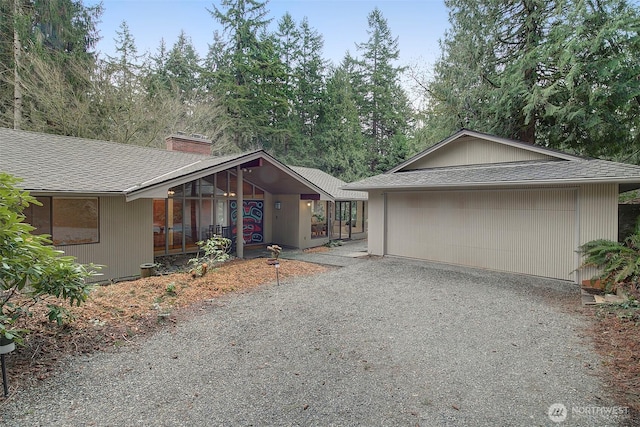 view of front of property featuring gravel driveway, roof with shingles, an outdoor structure, and a chimney