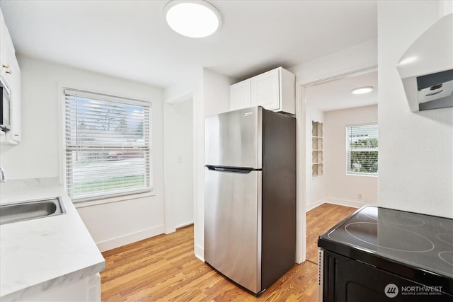 kitchen with light wood-type flooring, a sink, freestanding refrigerator, and black electric range oven