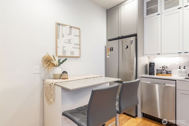 kitchen with light wood finished floors, dishwasher, glass insert cabinets, a kitchen breakfast bar, and light countertops