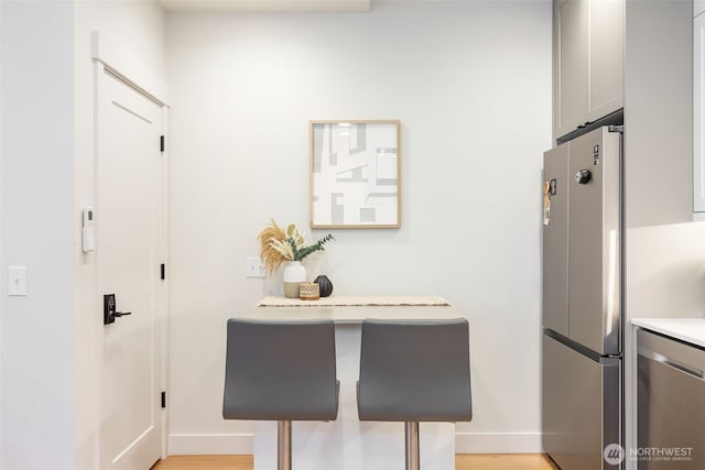 kitchen featuring stainless steel appliances, light wood finished floors, light countertops, and baseboards