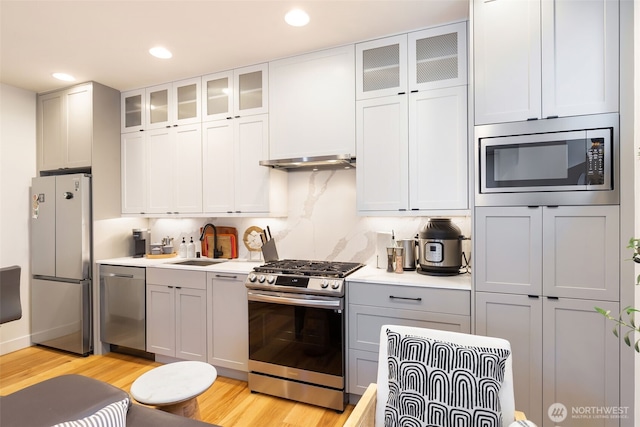 kitchen featuring stainless steel appliances, a sink, light countertops, light wood finished floors, and glass insert cabinets