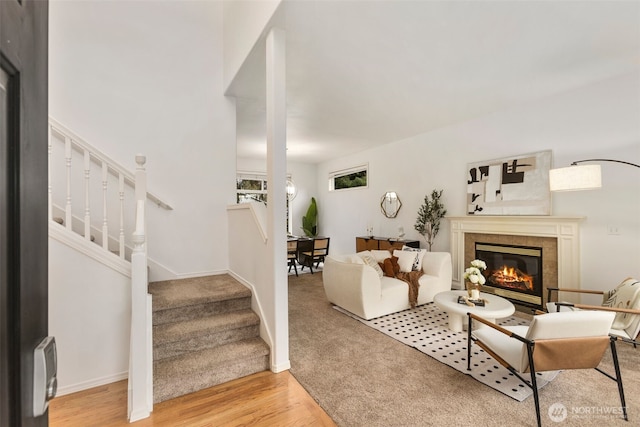 living area featuring stairway, a tiled fireplace, light wood-style flooring, and baseboards