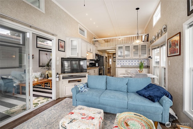 living area featuring a healthy amount of sunlight, ornamental molding, vaulted ceiling, and wood finished floors