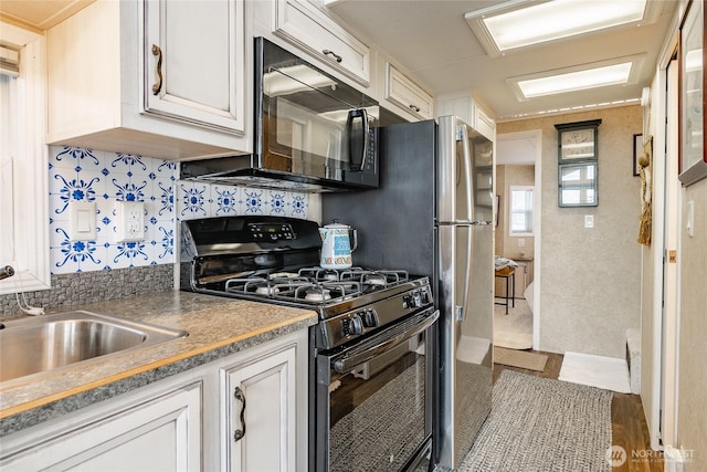 kitchen featuring black appliances, tasteful backsplash, white cabinetry, and a sink