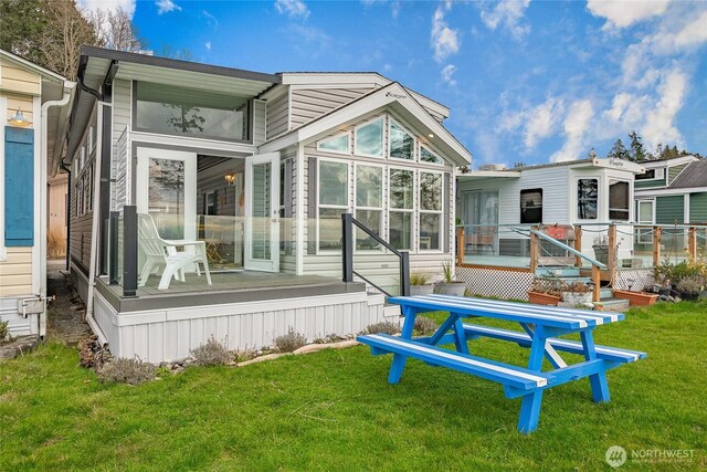 back of house featuring a deck, a lawn, and a sunroom