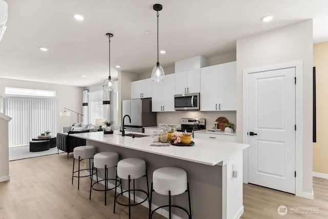 kitchen featuring an island with sink, appliances with stainless steel finishes, a breakfast bar area, light wood-style floors, and white cabinetry