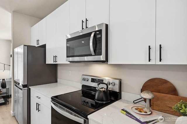 kitchen with stainless steel appliances, light wood-type flooring, white cabinetry, and light stone counters