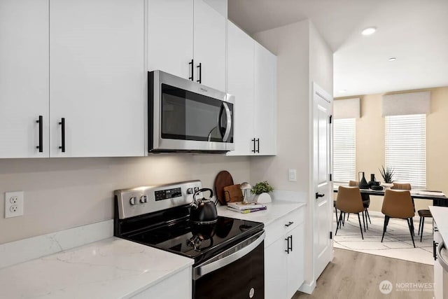 kitchen featuring light stone counters, light wood finished floors, stainless steel microwave, white cabinets, and range with electric cooktop