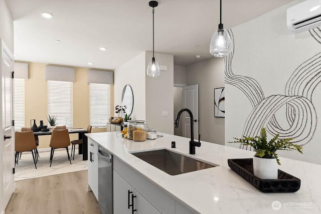 kitchen with a sink, light wood-style floors, an AC wall unit, stainless steel dishwasher, and decorative light fixtures