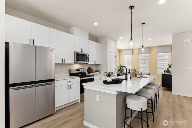 kitchen featuring a breakfast bar area, light wood-style flooring, a kitchen island with sink, stainless steel appliances, and white cabinets