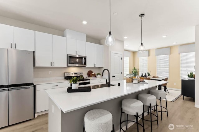 kitchen with white cabinets, appliances with stainless steel finishes, a kitchen island with sink, a kitchen bar, and a sink