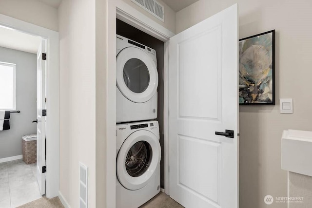 laundry room featuring laundry area, light tile patterned floors, baseboards, visible vents, and stacked washing maching and dryer