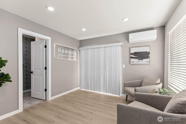 sitting room featuring baseboards, an AC wall unit, light wood-style flooring, and recessed lighting