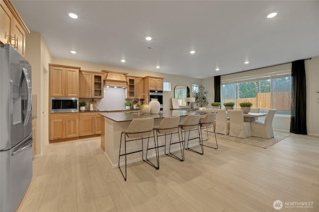 kitchen with light wood-style flooring, stainless steel appliances, premium range hood, a breakfast bar, and an island with sink