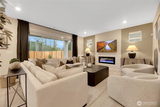 living room with light wood-type flooring, a glass covered fireplace, and recessed lighting