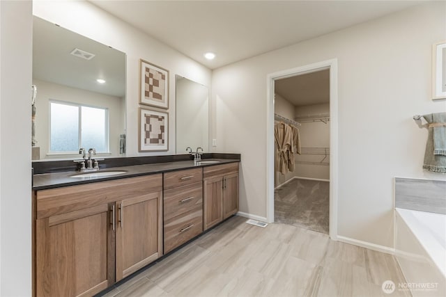 full bathroom featuring double vanity, a spacious closet, a sink, and a tub