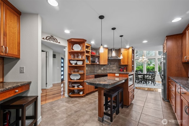 kitchen featuring a breakfast bar area, open shelves, decorative backsplash, appliances with stainless steel finishes, and wall chimney range hood