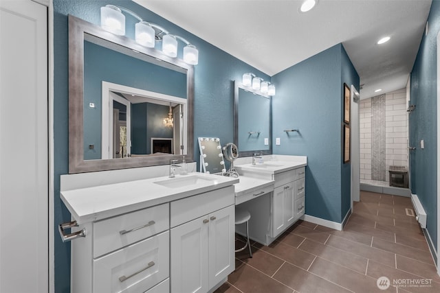 bathroom with tiled shower, two vanities, a sink, and baseboards