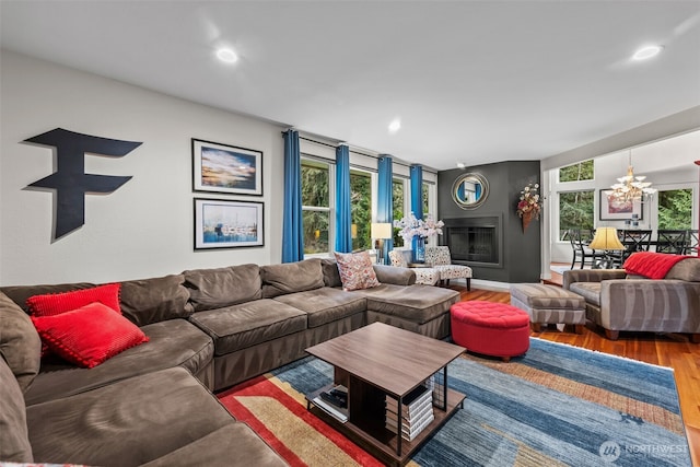 living area with a glass covered fireplace, an inviting chandelier, recessed lighting, and wood finished floors