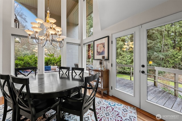 dining room with light wood-type flooring, an inviting chandelier, a towering ceiling, and french doors