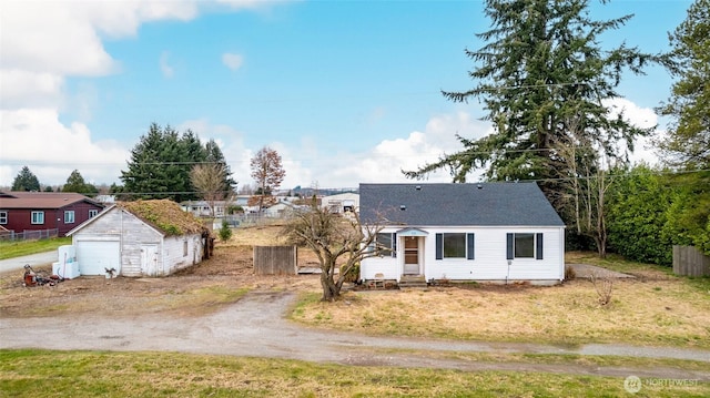 view of front facade featuring a detached garage, dirt driveway, a shingled roof, entry steps, and fence