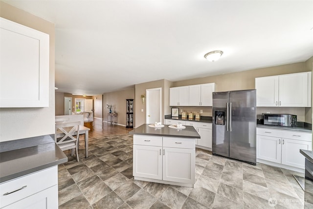 kitchen featuring a kitchen island, dark countertops, white cabinets, and stainless steel fridge with ice dispenser