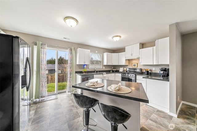 kitchen featuring a sink, a kitchen breakfast bar, dark countertops, white cabinetry, and stainless steel appliances